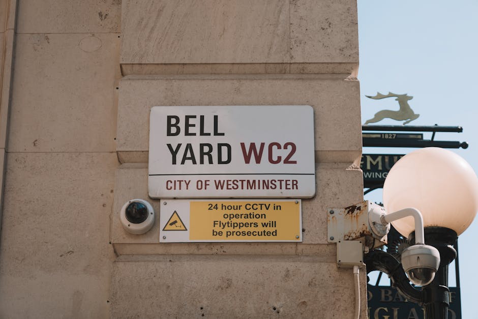 A close-up view of a beige stone wall featuring a street sign for the Bell Yard WC2 area in Westminster, London. Below the sign, there is a small security camera with a white dome casing positioned on